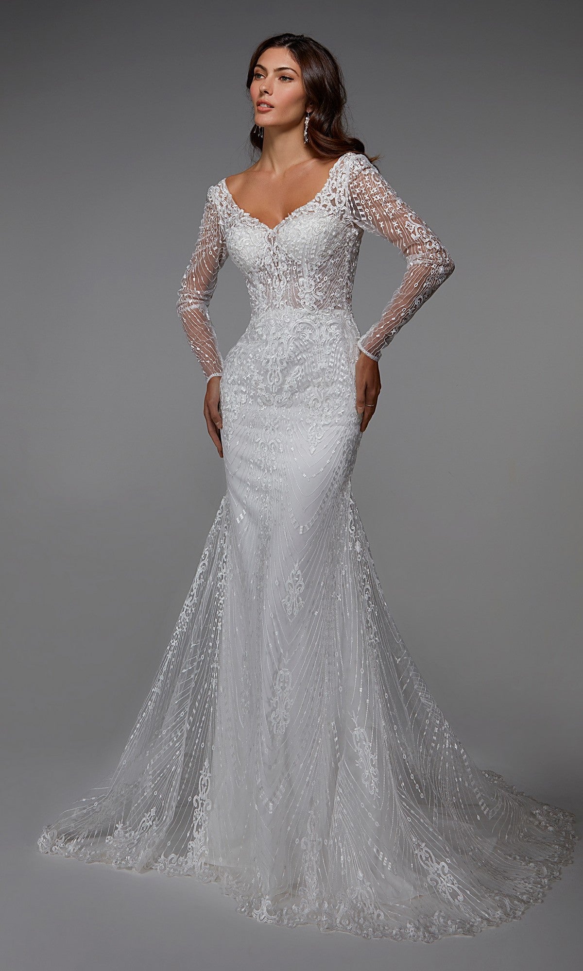 A woman in the Alyce 7030 long formal dress—an ivory, embroidered, long-sleeved lace sheath gown with a flowing train—stands against a plain gray background.